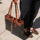 Bolso tipo tote de cuero color marrón con detalles en negro. Tiene doble asa de hombro y correa extraíble regulable. Incluye cierre principal y bolsillo interior.