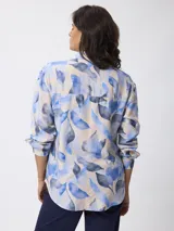 Camisa de manga larga con cuello clásico y cierre frontal de botones. Presenta un estampado de hojas en tonos azules sobre fondo claro y un bolsillo frontal en el pecho.