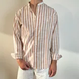 Camisa de manga larga con cuello mao, confeccionada en tejido de lino con estampado de rayas verticales en tonos amarillo y blanco. Presenta cierre frontal con botones y un pequeño bordado en el pecho.