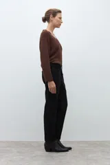 Pantalón negro de vestir, corte recto y tiro alto, con pliegues frontales y puños doblados. Se complementa con un cinturón fino negro con hebilla metálica en forma de símbolo.