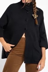Cardigan negro de corte oversize, con cuello alto, cierre frontal de botones y mangas tres cuartos. Presenta un diseño holgado con bolsillos frontales y una caída fluida.