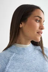 Buzo de tejido de punto con cuello redondo, diseño cropped y mangas largas con puños acanalados. Presenta una textura jaspeada en tono beige.