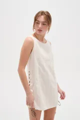 Vestido corto de algodón color blanco, de corte holgado, sin mangas y con cuello a la base. Presenta detalles de cordones cruzados y ojalillos en los laterales.