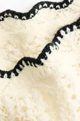 Pollera mini playera de punto crochet color blanco, de tiro bajo con tiras finas ajustables en los laterales y ribetes festoneados negros en contraste.