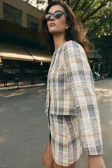 Blazer de cuello redondo y manga larga, con diseño a cuadros en tonos beige, azul y negro. Presenta cierre frontal cruzado con botones metálicos y corte recto.