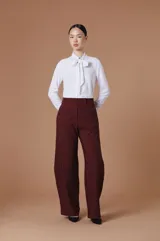 Blusa blanca de manga larga con cuello alto y detalle de lazo frontal tipo moño. Confeccionada en tejido ligero y fluido con corte entallado.