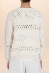 Suéter de punto calado color beige, de corte holgado y caída natural. Presenta un cuello redondo y mangas largas, ligeramente abullonadas, con detalles de calado y bordes festoneados.