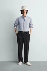 Camisa de algodón de corte relajado, con cuello solapa abotonado (button-down) y manga larga terminada en puño con botón. Presenta un patrón de rayas verticales finas en tonos azul claro y blanco.