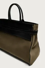 Bolso shopper de mano combinando cuerpo de gamuza color verde militar con solapa superior, asas y detalles en cuero sintético negro. Cuenta con compartimento principal con cierre imantado, bolsillo interior con cierre y bolsillo frontal plano con solapa.