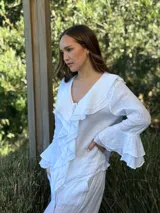 Camisa de lino azul marino con volados en cascada a lo largo del frente y en los puños de las mangas largas. Presenta un escote en V con un botón de nácar visible.