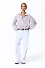 Camisa de algodón color lila, con cuello camisero ribeteado en encaje, cierre frontal de botones con detalles de encaje a los lados y mangas globo largas con puños elásticos.