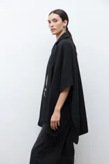 Capa negra con solapa y cuello tejido, de corte amplio y sin mangas.