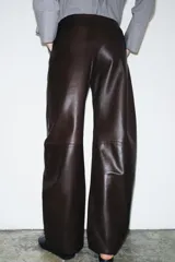 Pantalón de tiro medio con diseño tipo balloon, confeccionado en tejido efecto piel. Presenta bolsillos laterales, pespuntes marcados a tono y cierre frontal con cremallera, botón y gancho metálico.