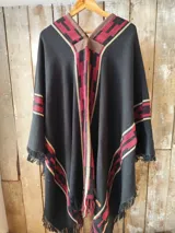 Poncho negro de hilo de algodón, con diseño geométrico tejido en tonos bordó y beige, detalles en cuerina marrón en el cuello y flecos en el ruedo.