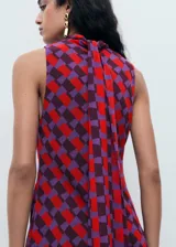 Vestido corto sin mangas con cuello alto, confeccionado en tejido estampado con patrón geométrico en tonos rojos y violetas.