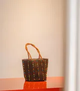 Cartera tipo tote de gamuza color marrón, con correas trenzadas y detalle de piedras naturales incrustadas en líneas verticales. Cuenta con cierre metálico y forro interior de tela.