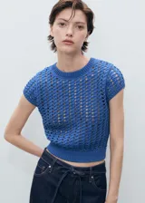 Jersey de manga corta confeccionado en tejido de punto grueso con diseño de crochet. Presenta cuello redondo, corte recto y diseño crop con terminaciones en tejido acanalado.