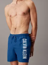 Short de baño de largo medio Calvin Klein, confeccionado en poliéster reciclado de secado rápido. Presenta cintura elástica con cordón ajustable, forro de malla interior, bolsillos laterales y un bolsillo trasero. Destaca por el logo de la marca estampado en vertical sobre la pierna.