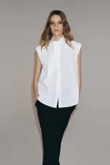Camisa sin mangas confeccionada en algodón, con cuello redondo y detalle de lazada frontal. Presenta cierre frontal con botones ocultos por solapa y bajo redondeado.