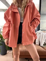 Campera color ladrillo con capucha, cierre frontal con cremallera y broches a presión, bolsillos laterales con solapa y puños elásticos.