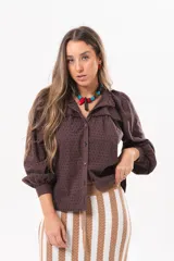 Camisa de broderie color marrón chocolate, con cuello alto, detalles de volados, mangas largas abullonadas y cierre frontal de botones.