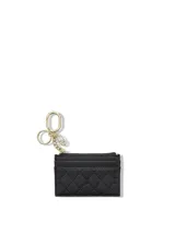 Tarjetero de cuero sintético negro con textura granulada y diseño acolchado en rombos, con cuatro ranuras para tarjetas, compartimento superior con cierre y llavero metálico dorado incorporado.