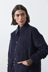 Campera capitoneada de algodón con diseño matelaseado, cuello camisero y cierre frontal con botones a presión. Presenta un corte relajado y bolsillos frontales.