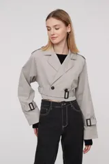 Trinchera corta color gris claro, con solapas, doble botonadura, cinturón y mangas largas con trabillas ajustables.