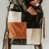 Bolso tipo tote de cuero vacuno con diseño patchwork en color negro, camel y blanco. Tiene correa de mano corta y correa larga ajustable para usar como morral. Cuenta con bolsillos verticales con cierre en ambos lados, bolsillo trasero con cierre y forro interior con bolsillo con cierre y bolsillo para celular.