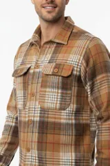 Sobrecamisa de franela a cuadros en tonos marrones, blancos y rojos, con mangas largas, bolsillos frontales con solapa y cierre de botones.