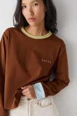 Remera de manga larga color marrón con cuello redondo en tono verde claro y puños en tono celeste. Presenta el logo de la marca bordado en el pecho.