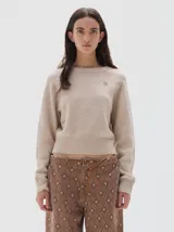 Buzo de tejido de punto color beige, con cuello redondo a la base, mangas largas y puños acanalados. Presenta un pequeño bordado de estrella en el pecho.
