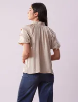 Blusa color beige de gasa con cuello fruncido, escote en V con lazo y mangas cortas con volados.