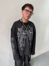 Remeron oversize de algodón pesado color negro con estampado gráfico en serigrafía gris en el frente y en ambas mangas. Presenta cuello redondo y grifa de la marca en el puño.