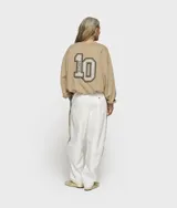 Suéter oversize de tejido de felpa de algodón y punto, color beige. Presenta cuello redondo, puños y bajo acanalados, y un bajo abullonado con detalle plisado y cordón ajustable.