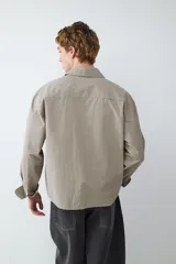 Camisa de mangas largas color beige con estampado a cuadros pequeños, corte boxy y cierre frontal con botones. Presenta cuello con solapa y un bolsillo de parche en el pecho.