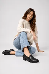 Mocasín clásico de cuero negro, con taco bajo y ancho de 4 cm. Combina laterales lisos con un panel frontal de acabado brillante y textura sutil, con una banda ancha sobre el empeine.