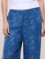 Pantalón palazzo de rayón color azul con estampado paisley blanco, corte amplio, tiro medio-alto con pretina elastizada y aberturas laterales en el puño regulables con lazos.