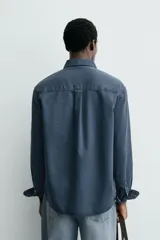 Camisa de corte relajado confeccionada en una mezcla de lyocell y algodón con efecto lavado. Presenta cuello solapa, manga larga con puños abotonados, bolsillo de plastrón en el pecho y cierre frontal con botones.
