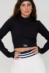 Top deportivo negro de manga larga, confeccionado en tejido acanalado, con cuello alto y cierre frontal parcial. Presenta un diseño ajustado tipo crop top con el logo 'bk.' estampado en el frente.