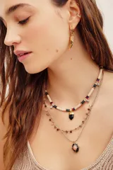 Collar corto tipo gargantilla de cuentas acanaladas de color beige con detalles multicolor y un dije colgante de piedra negra en forma de prisma con detalles dorados.