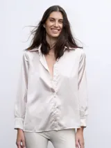 Camisa color beige de raso con cuello clásico, cierre frontal con botones y mangas largas con puños adornados con plumas.