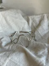 Brazalete rígido plateado con diseño irregular de ondas.