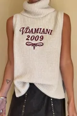 Chaleco tejido de punto en color beige, con cuello alto tipo polera y diseño sin mangas. Presenta un bordado frontal en color bordó con el texto 'Vdamiani 2009' y un detalle gráfico ornamental.