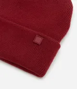 Gorro de punto de estilo beanie, color bordó, con borde plegado y etiqueta decorativa aplicada.
