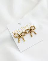 Aros colgantes dorados con forma de moño, hechos de pequeñas esferas de acero.