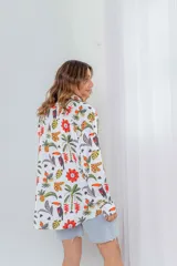 Camisa de seda blanca con estampado de flores rojas, palmeras, piñas y tucanes. Tiene cuello clásico, mangas largas y corte recto.