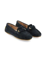 Mocasín de mujer confeccionado en gamuza color azul marino, con detalle de lazo en el empeine y aplique metálico dorado. Presenta suela de goma color suela con diseño de tacos.
