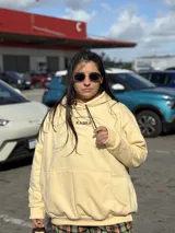 Canguro amarillo de corte holgado con capucha y cordones ajustables. Presenta el logo bordado en color marrón en el centro del pecho y un bolsillo frontal tipo canguro.