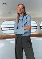 Pantalón de traje gris con sutil diseño de cuadros, tiro medio y pernera recta. Cuenta con trabillas para cinturón, pinzas delanteras, bolsillos laterales y cierre frontal con cremallera, botón y ganchos ocultos.